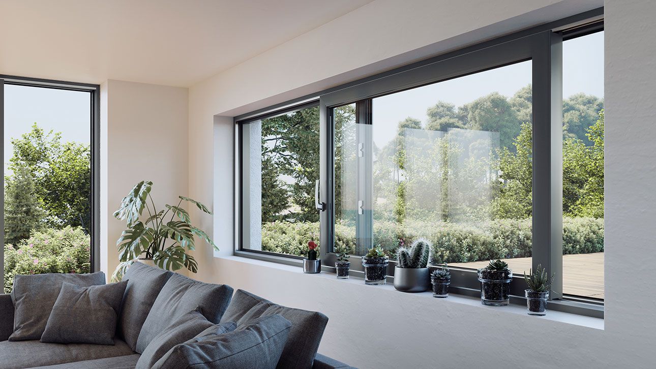 Wohnzimmer mit grauem Ecksofa, großen Fenstern und mehreren Pflanzen auf der Fensterbank